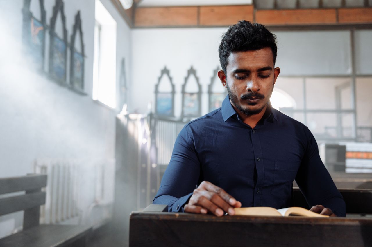 brand-02 A man in a blue shirt reads a book in a sunlit church, creating a serene atmosphere.