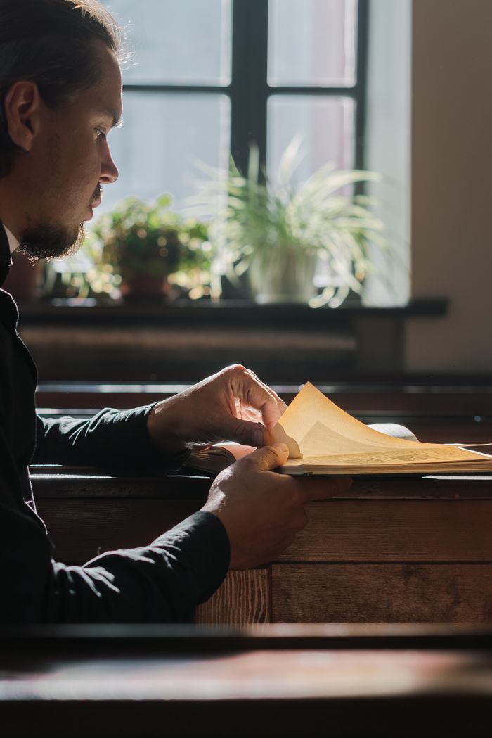 creative-02 Man in black clothes reading paper indoors beside a window in a church setting.